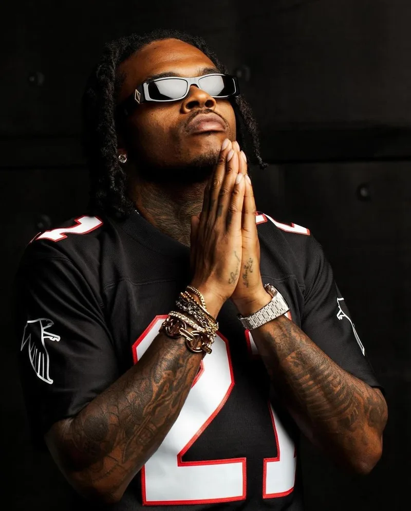 Gunna en maillot des Atlanta Falcons numéro 21, mains jointes, bracelets et tatouages