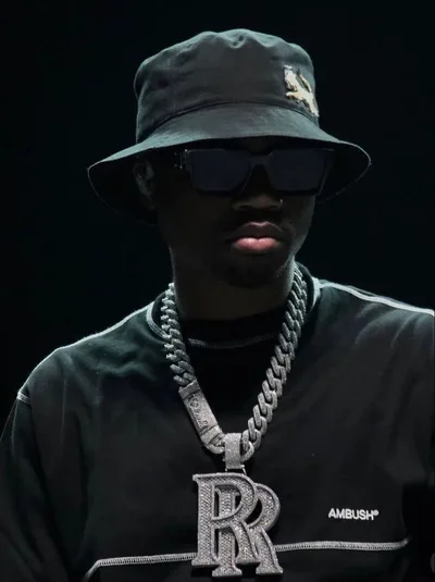 Roddy Ricch en bob et lunettes noires, pendentif RR, t-shirt AMBUSH sur fond sombre