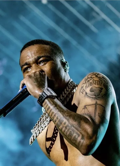 Roddy Ricch en concert sous les lumières, micro en main, tatouages sur le bras