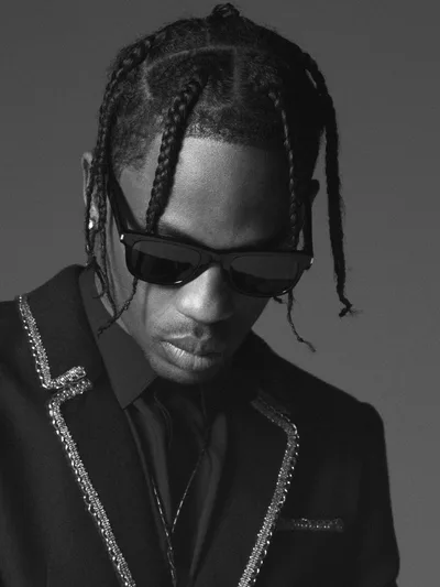 Travis Scott en veste à strass et lunettes noires, regard baissé, noir et blanc